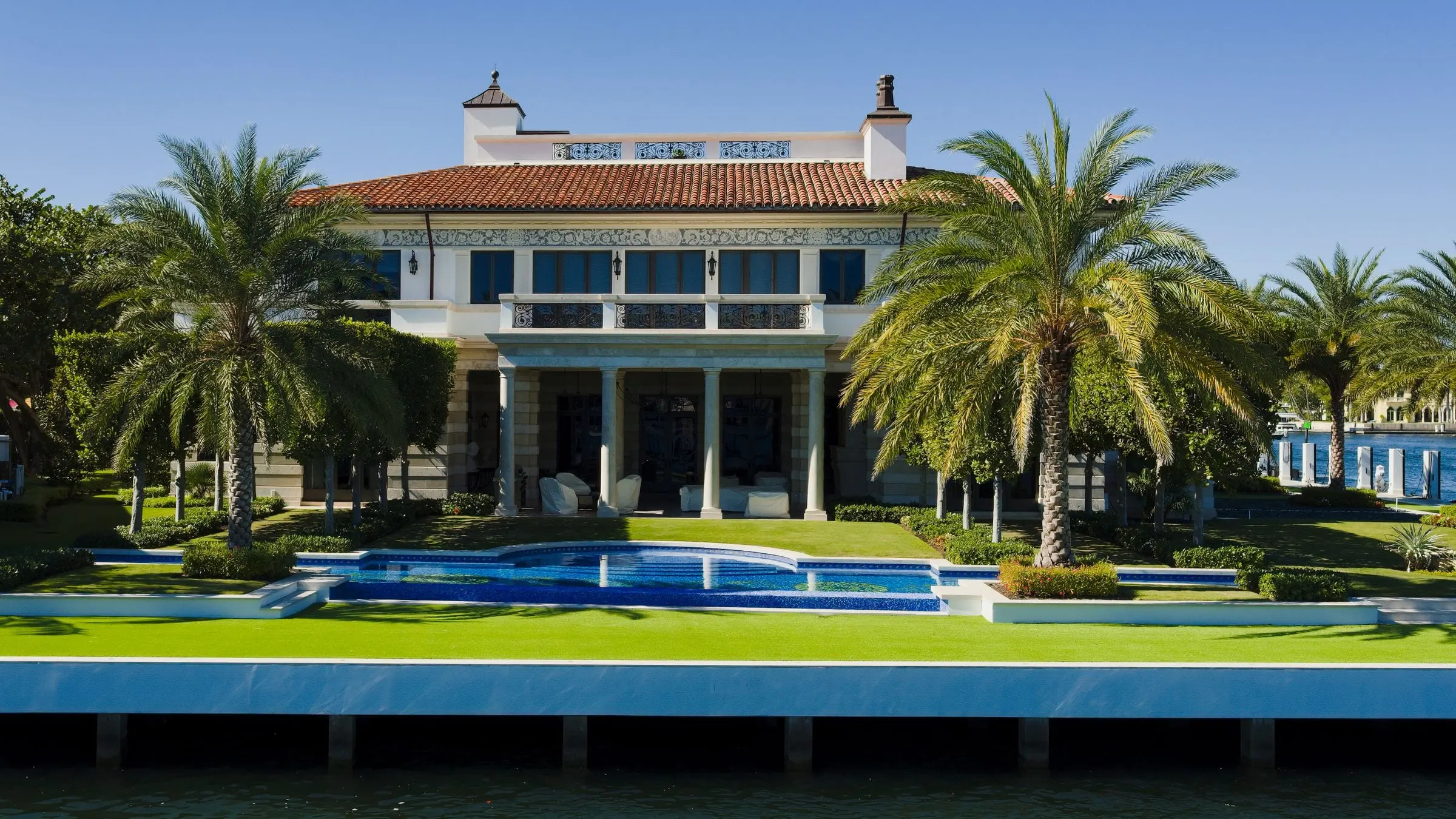 Large home with palm trees, a manicured lawn and a pool beside the water