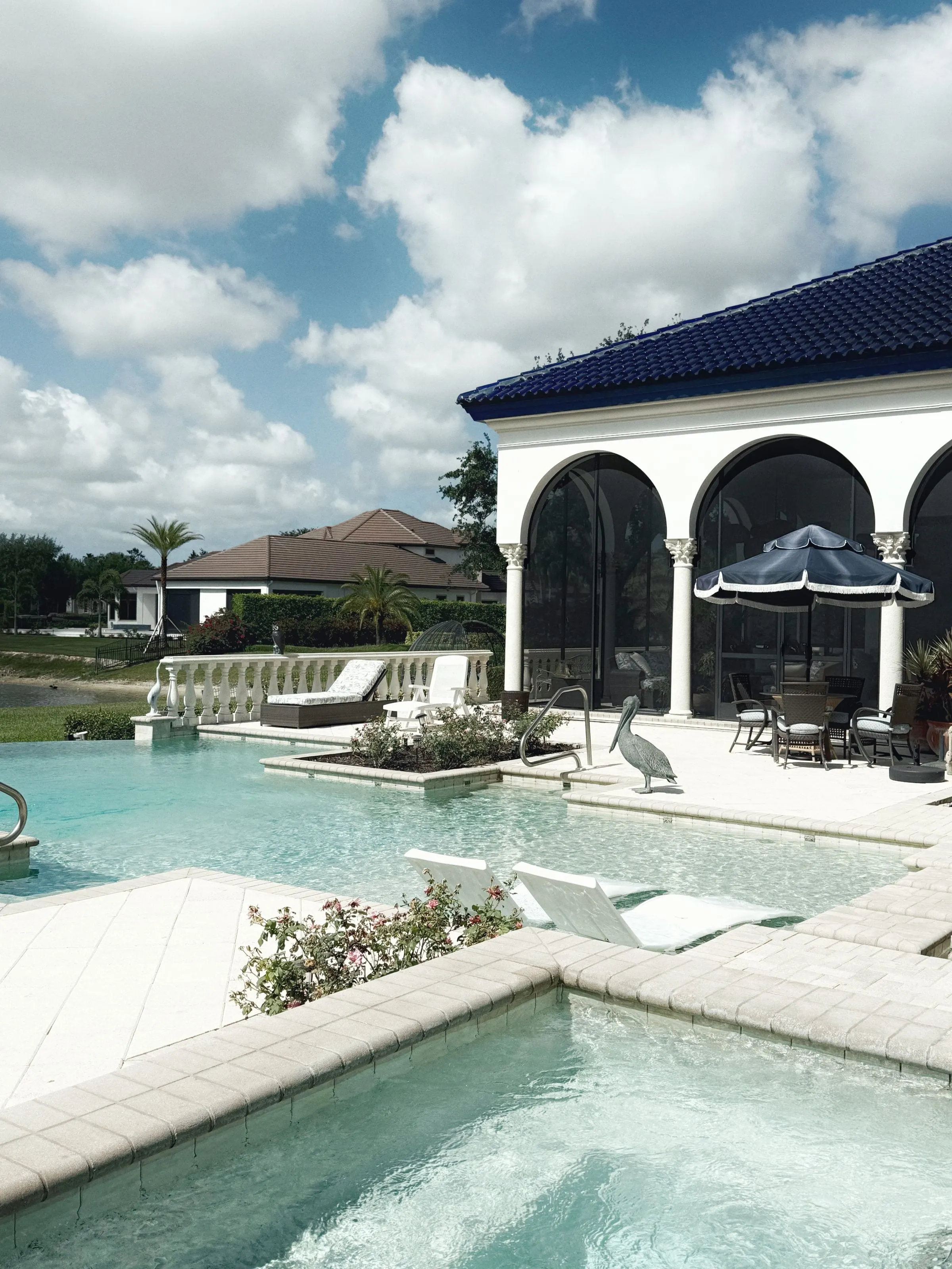 Pool and spa beside an arched covered patio under a bright sky