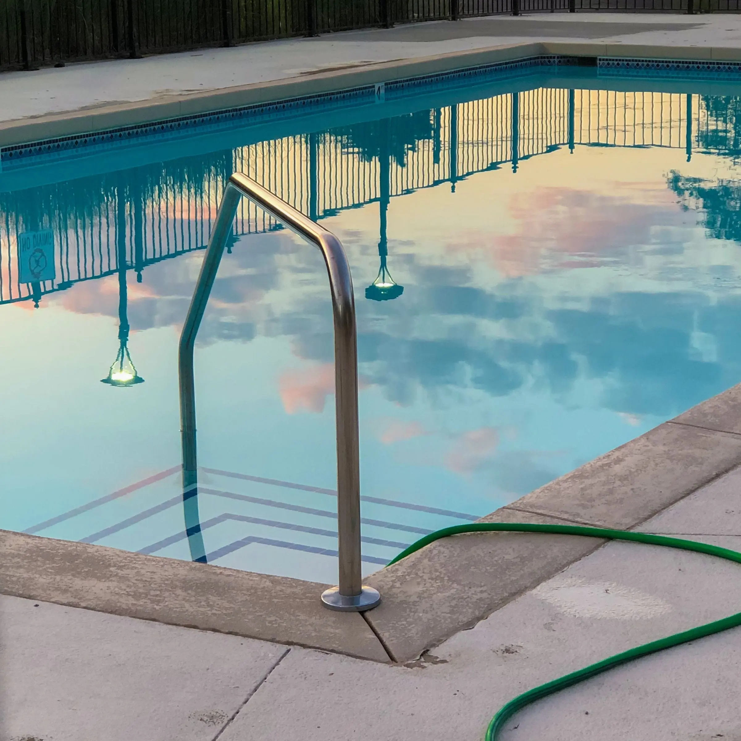 Pool ladder with clouds reflected in calm, clear water