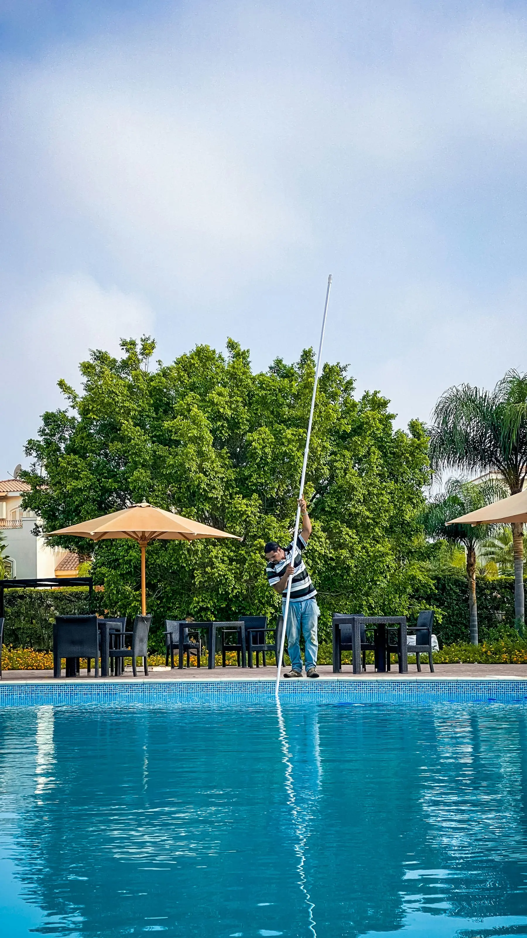 Pool technician skimming a bright blue pool with a long pole