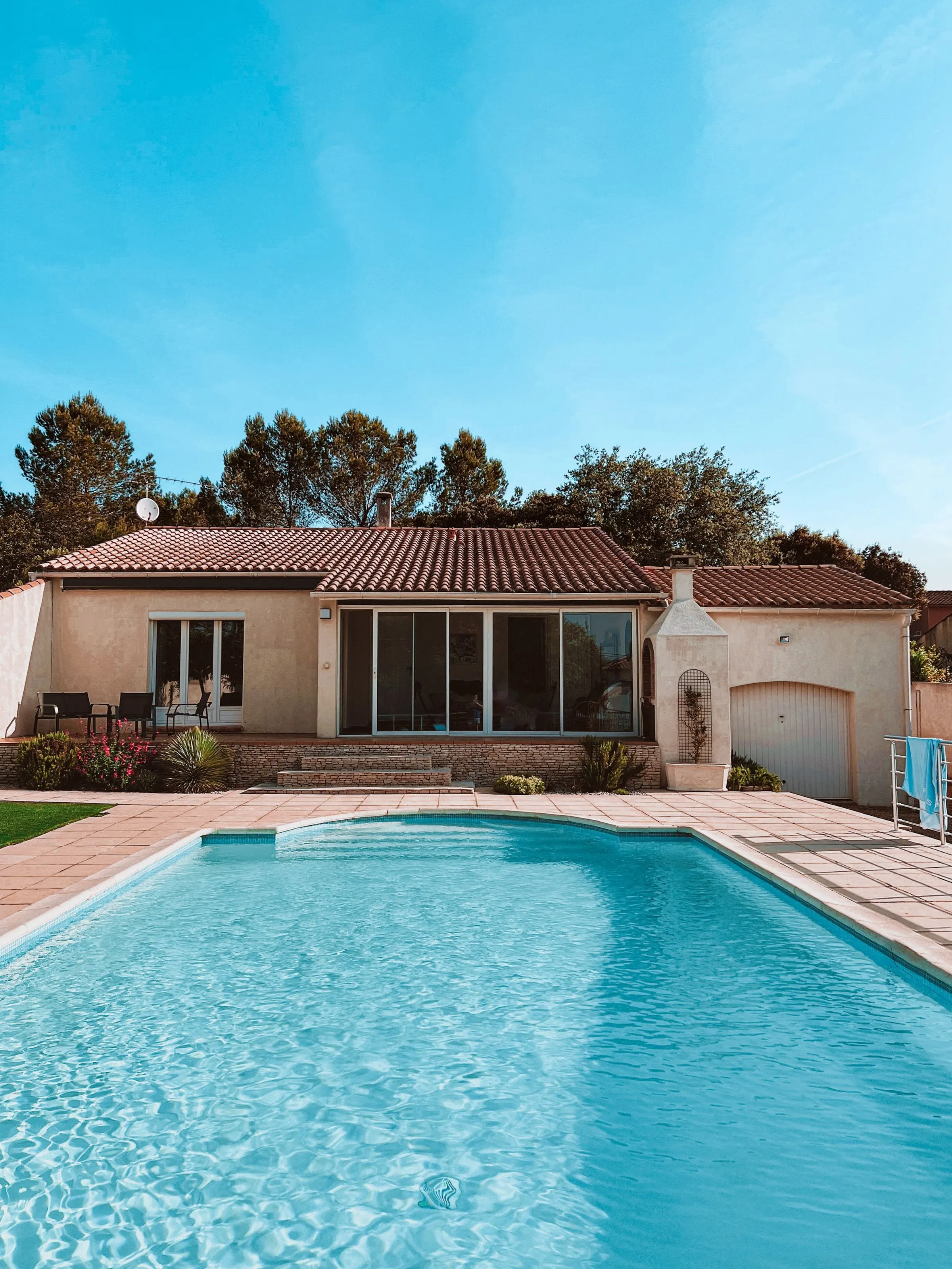 Single-story home with a tile roof behind a bright blue pool
