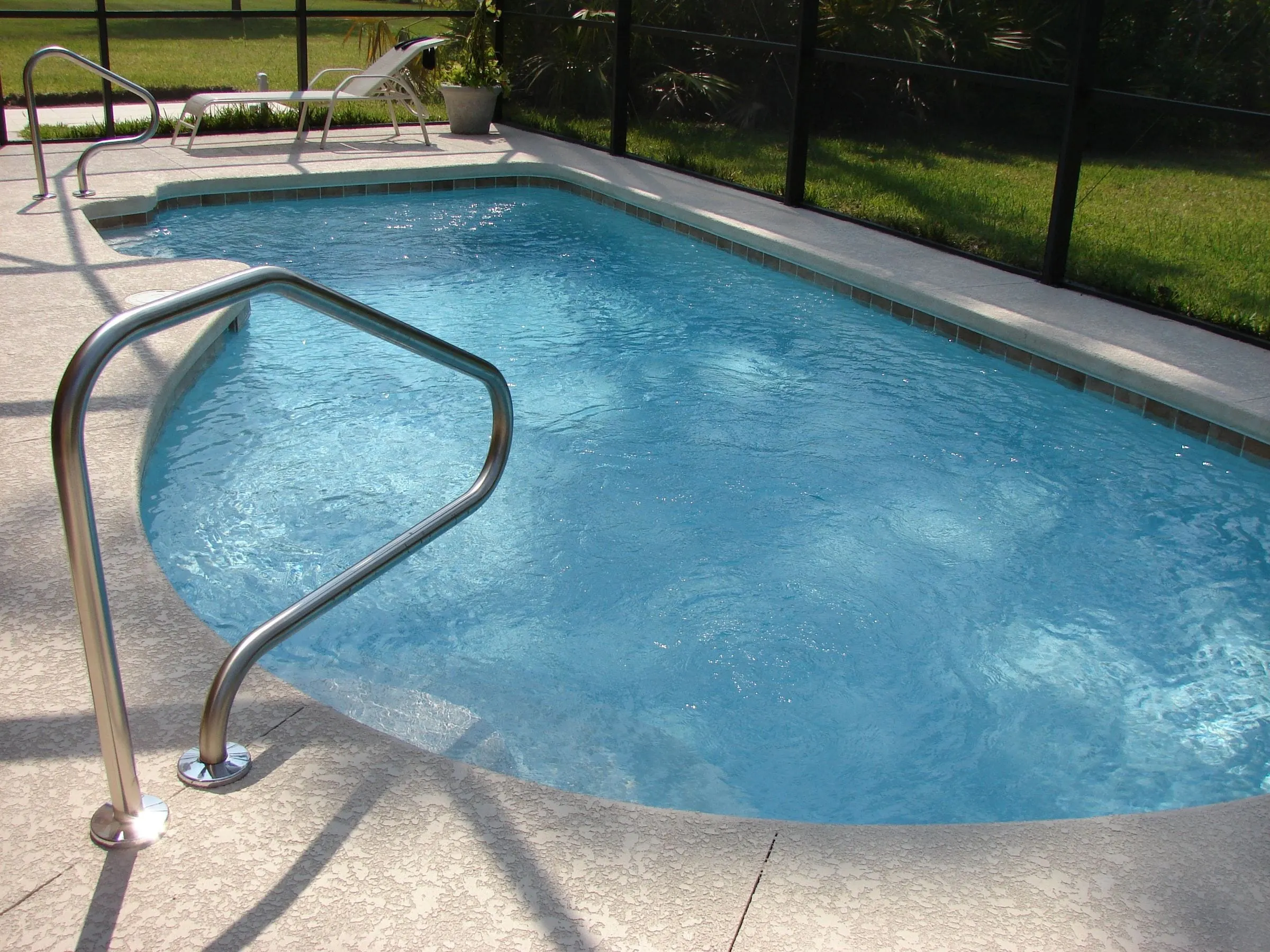 Clear blue pool with a stainless handrail inside a Florida-style screen enclosure