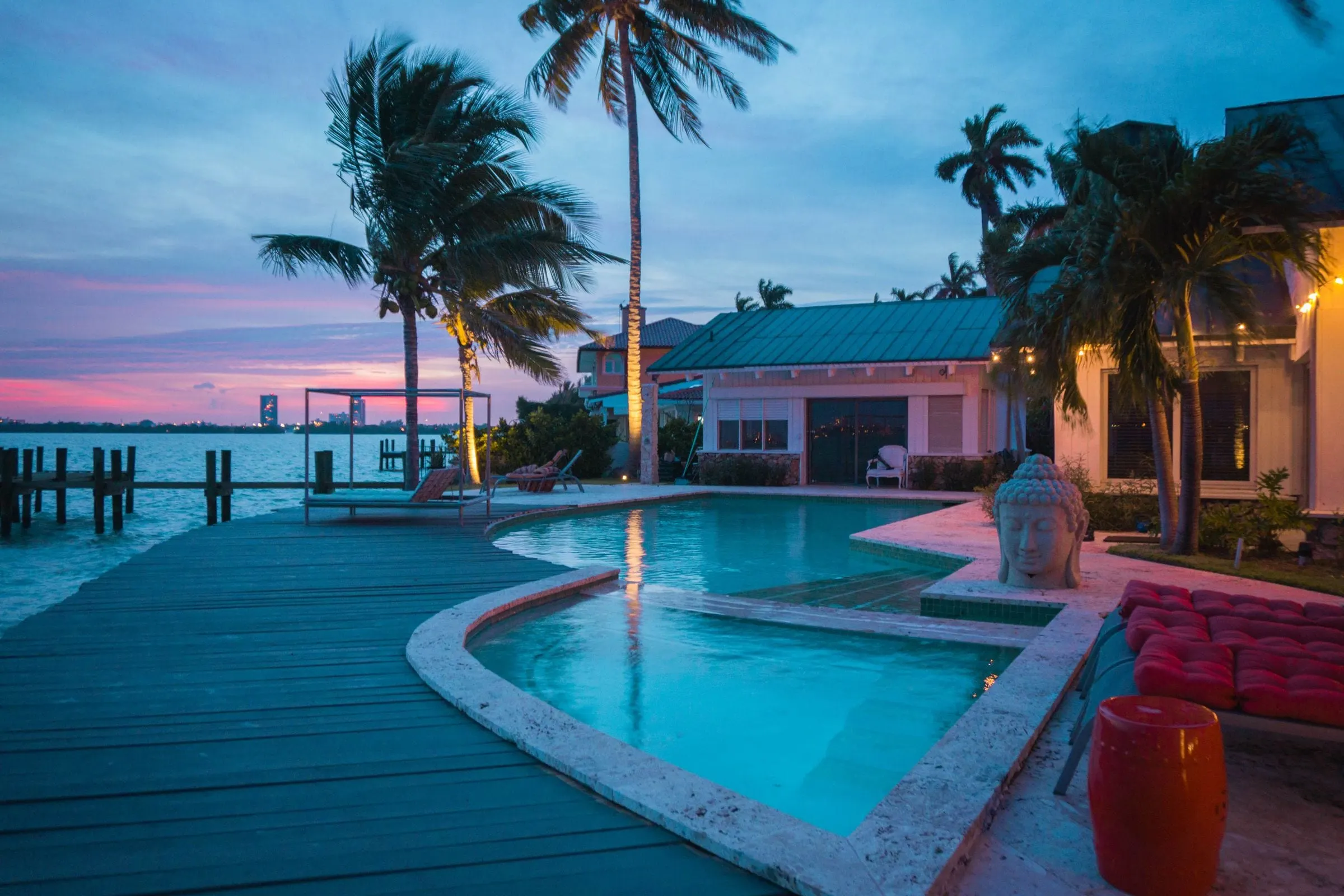 Pool beside a waterfront deck with palm trees at dusk